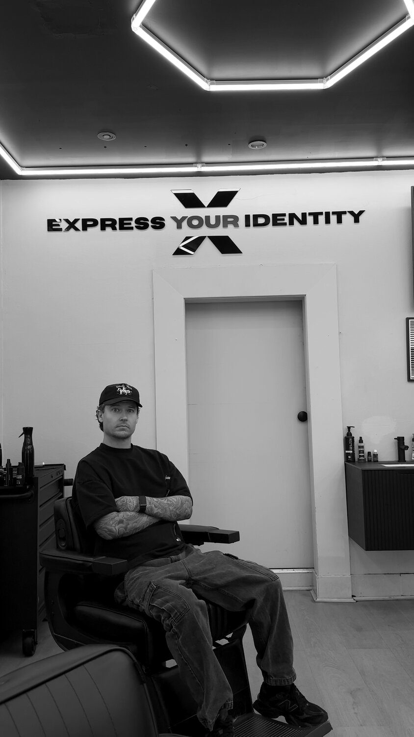 Jacob, director of Gallery X Barbershop, seated in the chair beneath the 'Express Your Identity' wall sign